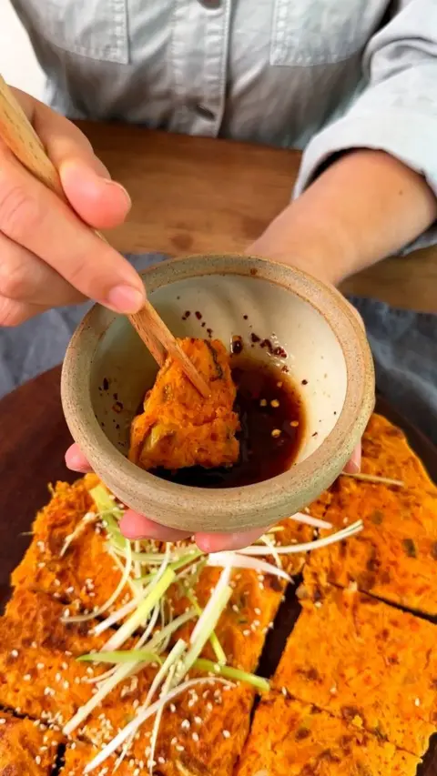 Somebody holding the Korean kimchi pancake with sticks and dipping it into sauce