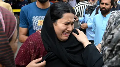 A mother wearing a black headscarf cries outside hospital surrounded by people showing her their support