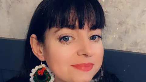 Jane Grandon Jane Grandon wearing red lipstick. She has earrings on and has black hair.