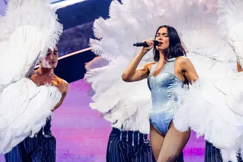 Getty Images Dua Lipa sings while dancers surround her with white feathered fans