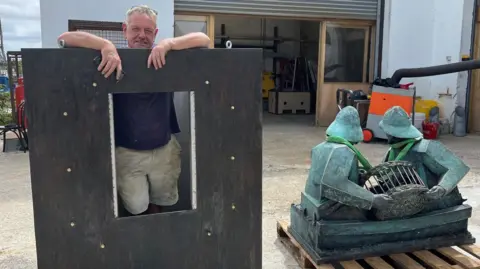 Tom stands next to his bronze sculpture inside the plinth where it will be mounted The plinth has a hole big enough for Tom to crawl into so the plinth can be bolted down