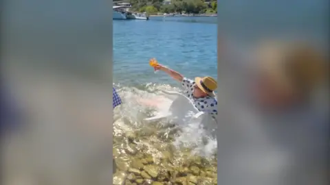 Alan carr falls into the water wearing a hat and clothes