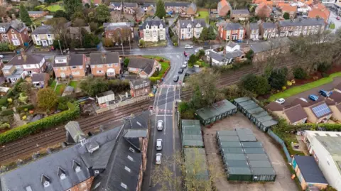 Aerial photograph of a railway crossing in a small town, with houses and industrial units in the background. 