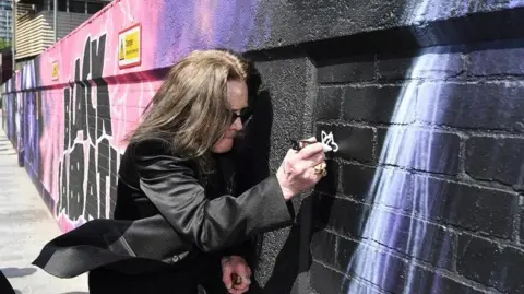Central BID Birmingham Ozzy Osbourne is pictured adding something in white to the mural, which goes from left to right on the photo.
