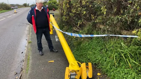 BBC Mabe parish councillor Peter Tisdale next to the chopped down speed camera