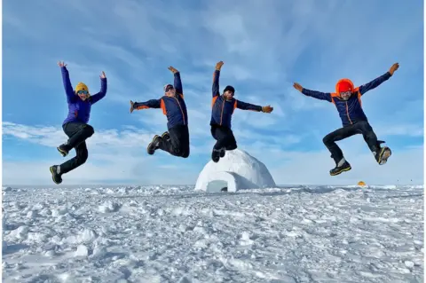 BBC Justin Rowlatt (right) jumping with colleagues and a scientist in Antarctica