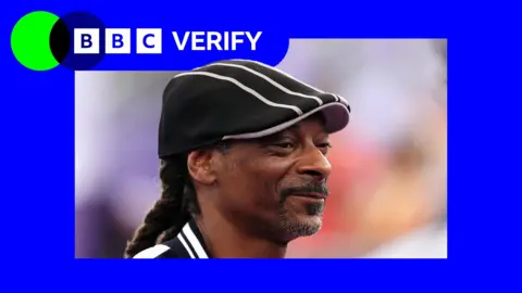 Rapper Snoop Dogg wears a black peaked cap with beige trim.