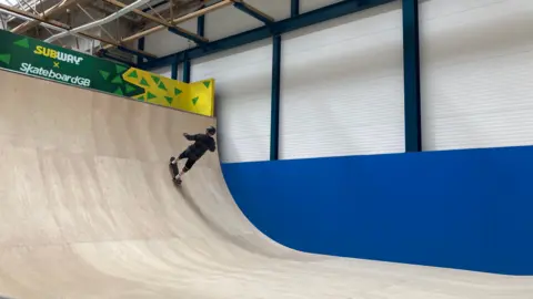 A silhouette of a skater heading up a large ramp indoors