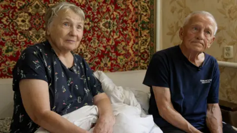 Francesco Tosto/BBC Dmytro's parents Halyna and Vasyl sit on their bed at home in the Kyiv region