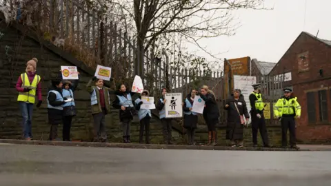 Children in high vis jackets holding posters stand on a pavement with police officers