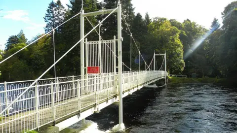 A white bridge over a river with green trees in the background. 