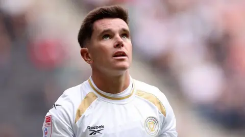 Liam Kelly in a white and gold MK Dons jersey during a match.