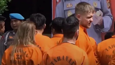 A group of people wearing orange boiler suits.