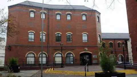 The exterior of Grimsby Crown Court - a modern three-storey red brick building with a wide stepped area leading up to its entrance. The sky is grey.