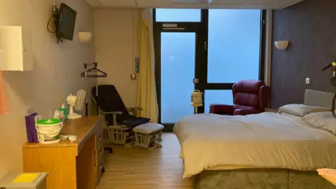 Charles Heslett/BBC A double bed inside a room with two purple chairs and a door and floor-to-ceiling window