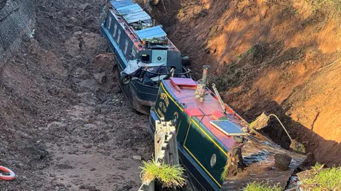 Narrowboats in a deep, muddy trench 