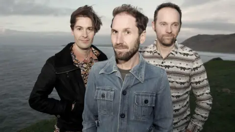 The band standing on a cliff by the sea in the Gower Peninsula.