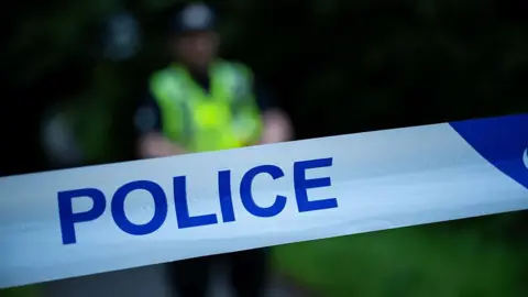 A stock image of police cordon. A police officer is blurry in the background. 