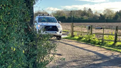 A police vehicle is parked at the entrance to a farm