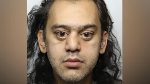 Asad Abbas, a man with shoulder-kength wavy black hair and brown eyes. 