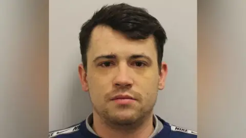 Met Police Jordan McSweeney mugshot. A white man with dark hair and eyes looking straight at the camera