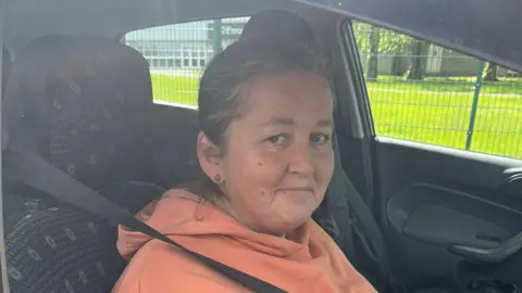 A woman sitting in the seat of a car wearing a seat belt and orange hoodie 