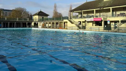 Vivacity Peterborough Large outdoor swimming pool with a two-storey green building in the background.