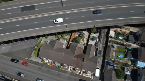 An overhead image from a drone showing how close to the M4 motorway the houses and gardens are. The image shows the motorway at the top of the image passing over the garden of a row of terraced houses