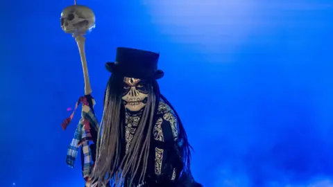 DCSDC Shows a skeletal figure in a black top hat and a staff with a skull