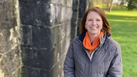 Harriet Eaton, Heritage Education Officer at Neath Port Talbot Council stands in Margam park wearing a grey coat and an orange scarf.