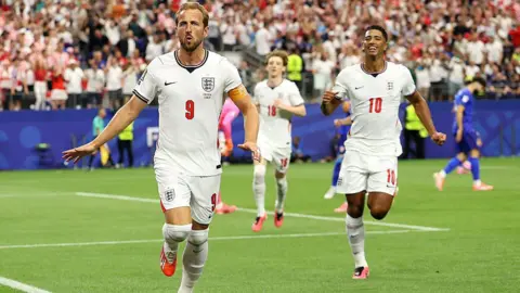 Harry Kane, England football player, celebrates after scoring a penalty for his team's first goal during the FIFA World Cup 2026 Group L match between England and Croatia at Dallas Stadium on June 17, 2026 in Arlington, Texas. Three players in England shirts are running forwards on a football pitch. 