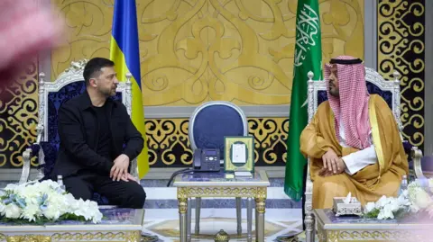 Reuters đưa tin: Tổng thống Ukraine Volodymyr Zelenskiy gặp Phó Thống đốc vùng Makkah, Hoàng tử Saud bin Mishaal bin Abdulaziz. Hai người ngồi trên những chiếc ghế cầu kỳ, giữa họ là một chiếc bàn mạ vàng bạc. Căn phòng họ đang ở rất sang trọng, với họa tiết in vàng đen trên tường. Ông Zelensky mặc bộ đồ đen toàn thân với áo khoác, còn Phó Thống đốc đội khăn trùm đầu truyền thống màu đỏ trắng.