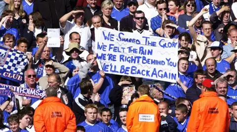 Getty Images Katie Worby in the crowd with her brother. Both are holding the banner above that reads: "We shared the glory. We've felt the pain. We're right behind you. We'll be back again".