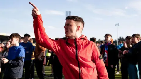 SNS An Inverness fan wearing a red jacket and standing in a crowd of fellow ITC supporters points angrily after the club was relegated.