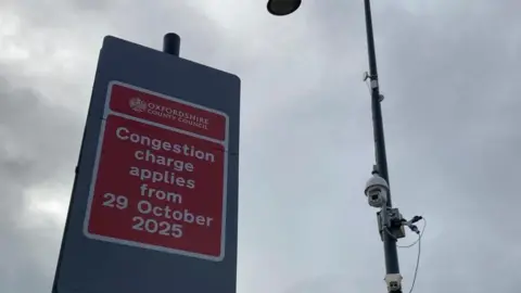 A congestion charge sign next to a number plate recognition camera.