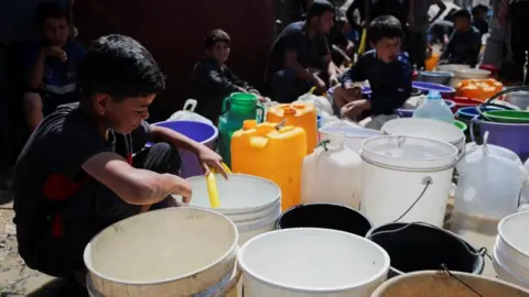 Palestinian children fill water containers at a refugee camp in Gaza City on Tuesday. One child is using a hosepite to fill a bucket.