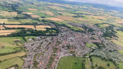 Joan Airey An aerial view of a village lined with residential houses and surrounded by green countryside.