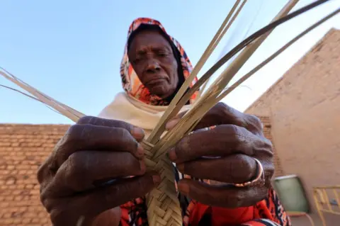 AFP A Sudanese woman weaves palm leaves (al-Zaaf), a traditional skill of making baskets, food trays and other household items, in the village of Al-Saqqai, some 57km north of the capital Khartoum, on January 4, 2023