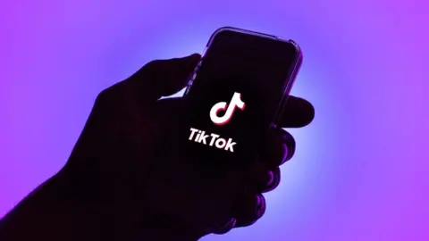 Getty Images An illustration of a hand holding a phone showing the TikTok logo