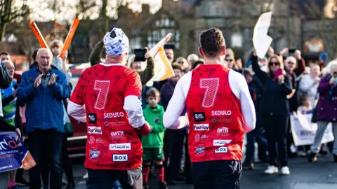 BBC/Poppy Jeffery View of the number 7 on the backs of Sinfield and his running teammate as they run through a crowd of well-wishers cheering and applauding on a residential street