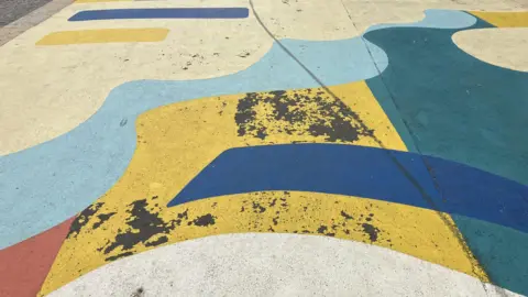 Image shows damaged sections of paint work on a colourful piece of street art. 