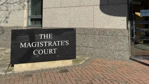 BBC The Magistrate's Court sign outside a grey building and a revolving door to the right.