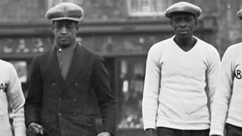 Getty Images Len Johnson wears a dark suit as he walks a dog in Manchester in December 1926 alongside his father and manager Bill Johnson, who wears a white jumper