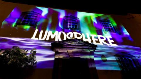 A building with purple, green and blue projections and the Lumosphere logo