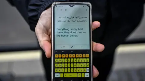 Getty Images A hand holding a phone that has translated a message into English. It reads: "Everything is very bad there, they don't treat us like human beings"