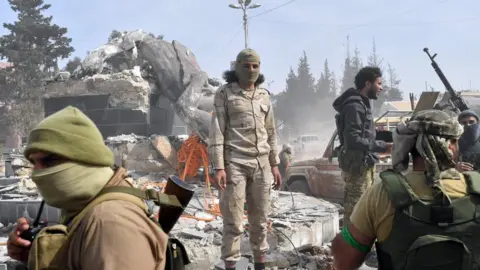 AFP Turkish-backed Syrian rebels gather next to the destroyed Kawa statue in the city of Afrin in northern Syria on March 18, 2018