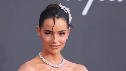 Getty Images Maura smiling. She is wearing a diamond necklace and has her dark brown hair tied back.