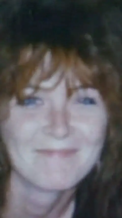 A blurry photo of a woman with brown hair smiling at the camera