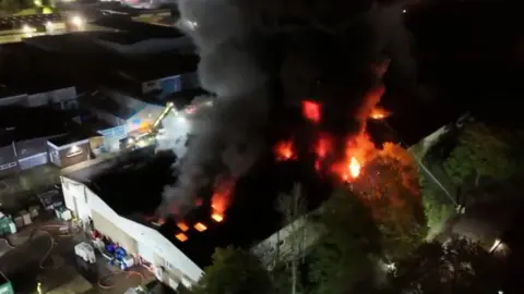 Aerial view of large recycling centre fire at night with flames and thick black smoke rising into the air