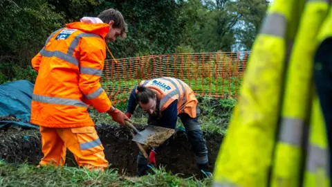 Fountains Media Two men wearing hi-vis jackets digging a trench in a field.